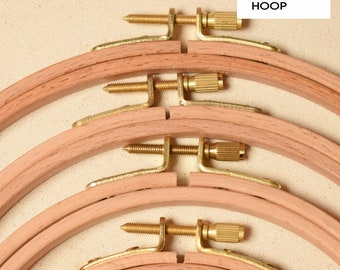 May include: Four wooden embroidery hoops of different sizes with brass screw tightening mechanisms. The hoops are stacked on top of each other.  WOODEN HOOP is written in white text on a black rectangle.