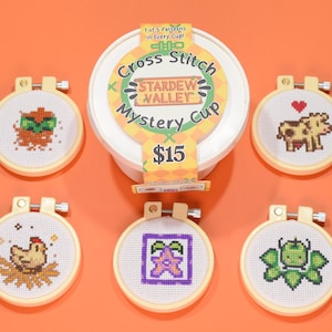 Puede incluir: Cinco pequeños aros de bordado blancos con diferentes patrones de punto de cruz del videojuego Stardew Valley. Los aros están sobre una superficie naranja brillante. El texto en el contenedor dice "Cross Stitch Stardew Valley Mystery Cup 15 €".