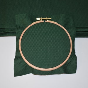 Op de afbeelding: Een groene stof gespannen over een ronde houten borduurring. De ring heeft een diameter van ongeveer 20 cm.