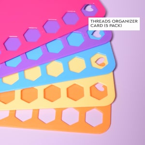 May include: A stack of colorful thread organizer cards in pink, purple, blue, yellow, and orange. Each card has a series of hexagonal cutouts and heart-shaped openings. The text "THREADS ORGANIZER CARD (5 PACK)" is visible.