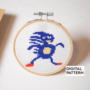 May include: A cross-stitch pattern of Sonic the Hedgehog running, framed in a wooden hoop. The pattern is in blue, yellow, and red.