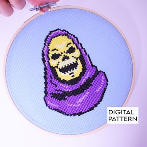 May include: A purple and yellow pixelated cross-stitch embroidery of Skeletor from the Masters of the Universe cartoon series. The embroidery is framed in a wooden hoop. The text "DIGITAL PATTERN" is visible in the bottom right corner of the image.