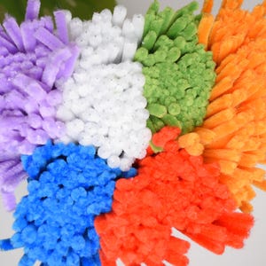 May include: A vibrant, abstract composition of craft materials. The image showcases a circular design with segments in shades of purple, white, green, orange, blue, and red. The texture appears soft and fluffy.