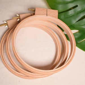 Puede incluir: Un conjunto de cuatro aros de bordado de madera, anidados entre sí. Los aros están hechos de madera natural y tienen un acabado liso. Los aros se utilizan para estirar la tela para el bordado.