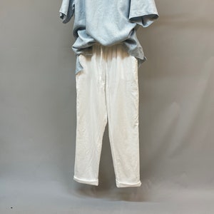 May include: A light blue linen shirt with a v-neck and a white linen pair of pants.