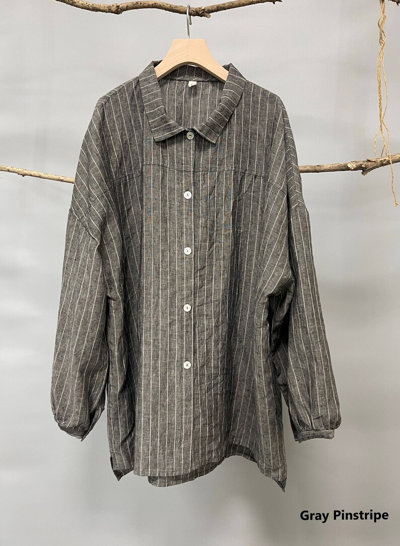 May include: Gray pinstripe button-down shirt with long sleeves. The shirt features vertical white stripes on a gray background. It has a collared neckline and white buttons. The shirt is hanging on a wooden hanger.