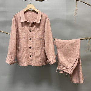Puede incluir: Conjunto de dos piezas de lino rosa claro, que incluye una chaqueta abotonada con dos bolsillos delanteros y pantalones a juego con cintura con cord&oacute;n. La chaqueta tiene mangas largas y botones de madera. El conjunto se exhibe en una percha de madera.