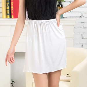 May include: White cotton slip skirt with a simple design. The skirt is knee-length and has a smooth, silky texture.
