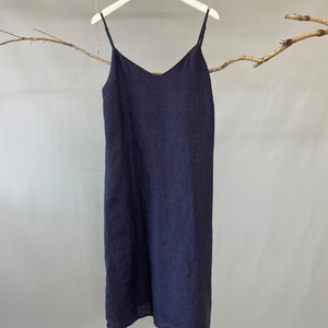 May include: A navy blue slip dress with thin spaghetti straps and a V-neck. The dress is made of a lightweight fabric and hangs on a white hanger. The dress is approximately knee-length.