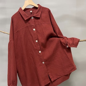 May include: Maroon button-down shirt with long sleeves, a classic collar, and white buttons. The shirt is made of a soft, textured fabric and hangs on a wooden hanger. The word "Maroon" is printed at the bottom right.