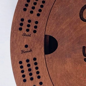 May include: A wooden game board with a circular track and holes for pegs. The board has the words "Start" and "Finish" inscribed on it.