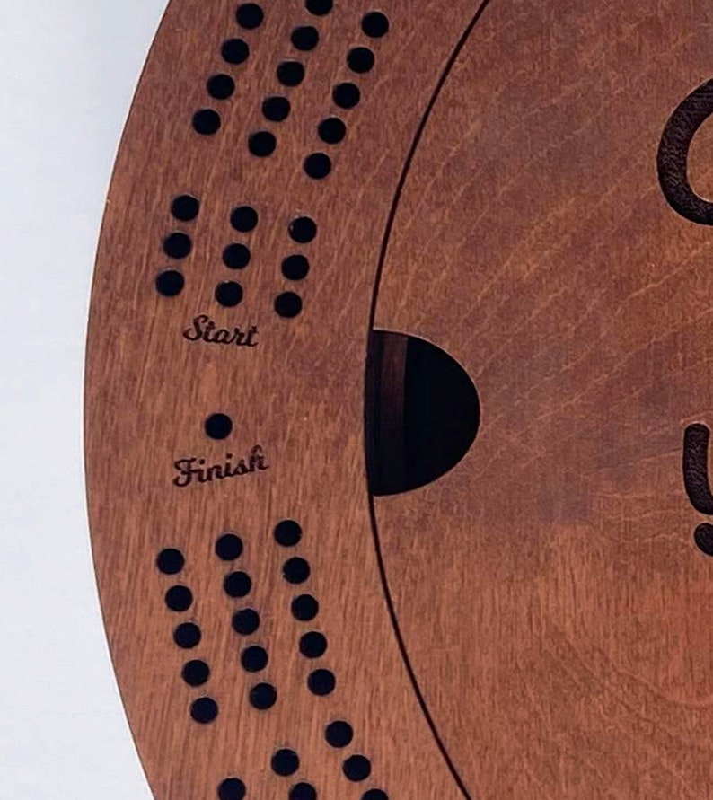 May include: A wooden game board with a circular track and holes for pegs. The board has the words "Start" and "Finish" inscribed on it.
