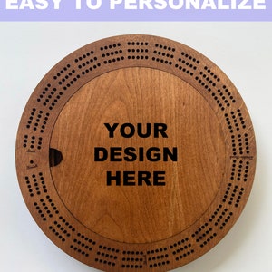 May include: A wooden cribbage board with a circular design. The board has a center section that can be personalized with a design. The text "YOUR DESIGN HERE" is printed on the board.
