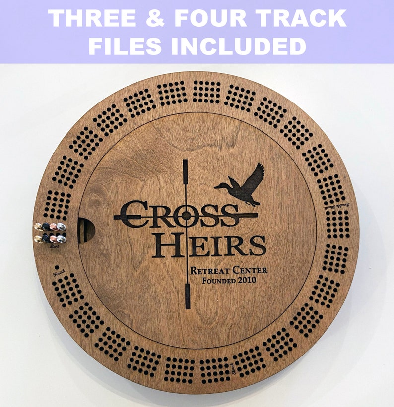 May include: A wooden game board with a circular design. The board has a black and white design with a duck and the words "Cross Heirs Retreat Center Founded 2010".