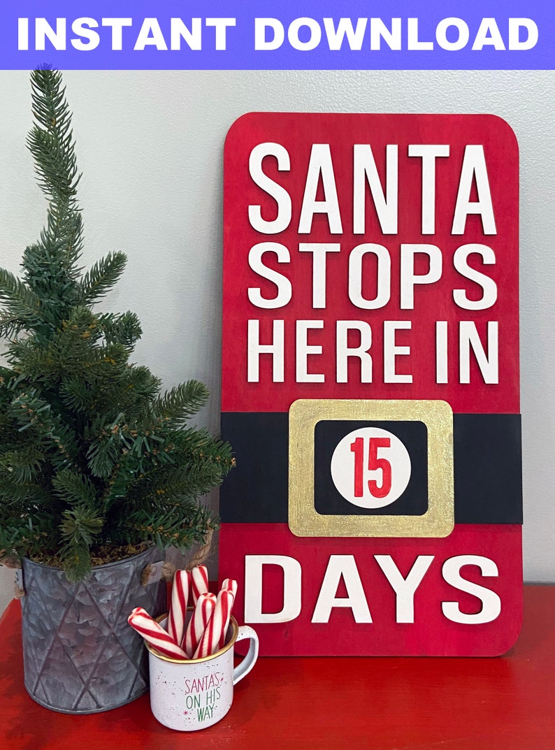 May include: A red wooden sign with white text that reads "Santa Stops Here In 15 Days". The sign is decorated with a black and gold belt with a white circle containing the number 15. The sign is sitting on a red table with a small potted tree and a mug with candy canes.