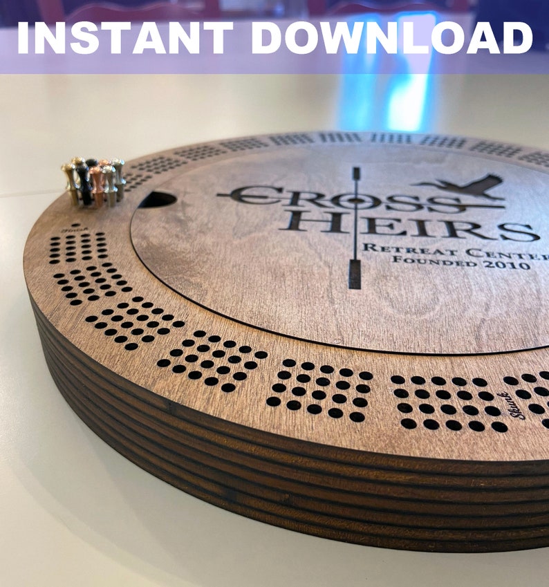 May include: A wooden game board with a circular design and a center section that lifts up. The board is engraved with the words "Cross Heirs Retreat Center Founded 2010".