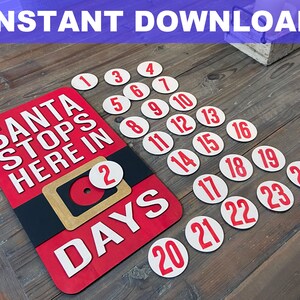 May include: A red and black Santa Claus countdown sign with the text "Santa Stops Here In" and a white circle with the number "2" on it. The sign also says "Days" in white letters. There are 24 white circles with red numbers on them, representing the days until Christmas.