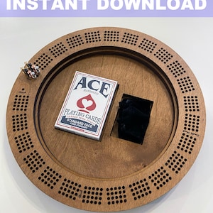 May include: A wooden cribbage board with a deck of playing cards and a small pouch. The board has a circular shape with a center hole and a ring of holes around the edge. The board is made of light brown wood and has a natural finish.