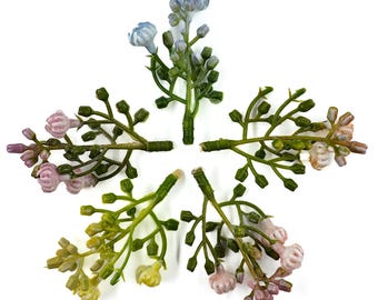 May include: Five artificial flower stems arranged in a star shape. The stems feature small, detailed flowers in shades of pink, yellow, and blue, with green leaves and stems. The flowers are set against a white background.