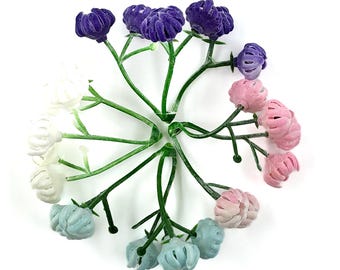 May include: A cluster of artificial flowers in a circular arrangement. The flowers are in shades of purple, pink, white, and blue, with green stems. The flowers have a textured, velvety appearance, and are set against a white background.