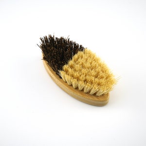 May include: A wooden-handled brush with two sides. One side has natural bristles and the other side has black bristles.