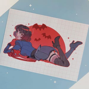May include: Illustration of a woman in a blue outfit, lying down with a red purse. A red moon with bat silhouettes is in the background. The artwork has a comic book style with a grid pattern.