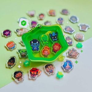 Peut inclure: Un présentoir en acrylique vert vif en forme d'étoile contenant six petites breloques de personnages colorées. Le boîtier comporte une chaînette à billes verte et le texte NEDIKUU.COM. De nombreuses autres breloques sont éparpillées.