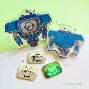 May include: Two blue robot-shaped acrylic charms, one featuring a circular slash icon on its screen. Three rectangular pins are included: one with a cowboy illustration, one with a smiling face, and one with a green-tinted character portrait.