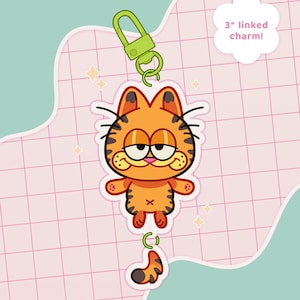 May include: A 3-inch linked charm featuring a cartoon orange tabby cat with a grumpy expression. The charm is attached to a green metal clasp.