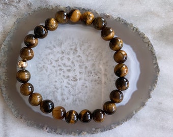 May include: A brown and gold tiger's eye beaded bracelet with a gold accent bead.
