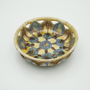 Peut inclure: Un bol en céramique avec un glaçage jaune et des motifs floraux bleus et bruns. Le bol a un bord ajouré.