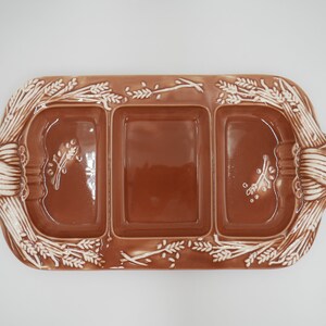 May include: A brown ceramic serving dish with three compartments. The dish is decorated with a white wheat design around the edge.