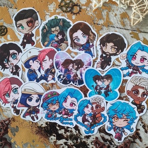 Op de afbeelding: Een verzameling van 15 kleurrijke cartoonfiguur stickers met verschillende personages met blauwe, rode, groene en gele accenten. De stickers bevinden zich op een houten oppervlak met een stervormig ontwerp.