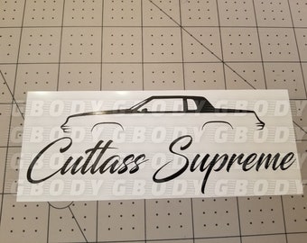 May include: A black and white sticker featuring a stylized outline of a car with the words "Cutlass Supreme" in a cursive font. The sticker is rectangular and appears to be on a white background.
