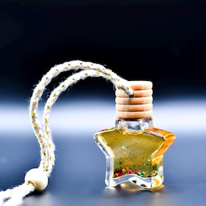 May include: A star-shaped car air freshener with a clear glass bottle filled with a golden liquid and colorful glitter. It has a wooden cap and a white and gold rope for hanging.
