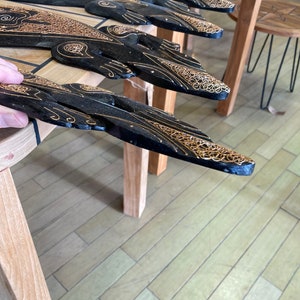 May include: Several black wooden decorative pieces with gold-colored intricate designs are arranged on a wooden table. The pieces have a curved shape and are likely part of a larger decorative set. The background includes wooden furniture and a light-colored floor.