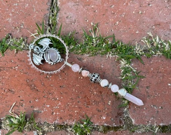 May include: A silver dragon charm with a pink crystal in the center, attached to a wand with pink crystal beads and a pink crystal point.