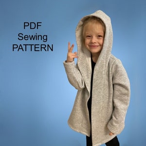 Może przedstawiać: Wzór szycia PDF na kardigan z kapturem o długim, swobodnym kroju. Kardigan jest jasnoszary i jest noszony przez dziecko.