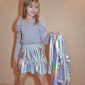 May include: A young person wearing a gray long-sleeved shirt with a silver iridescent skirt and a silver iridescent jacket.