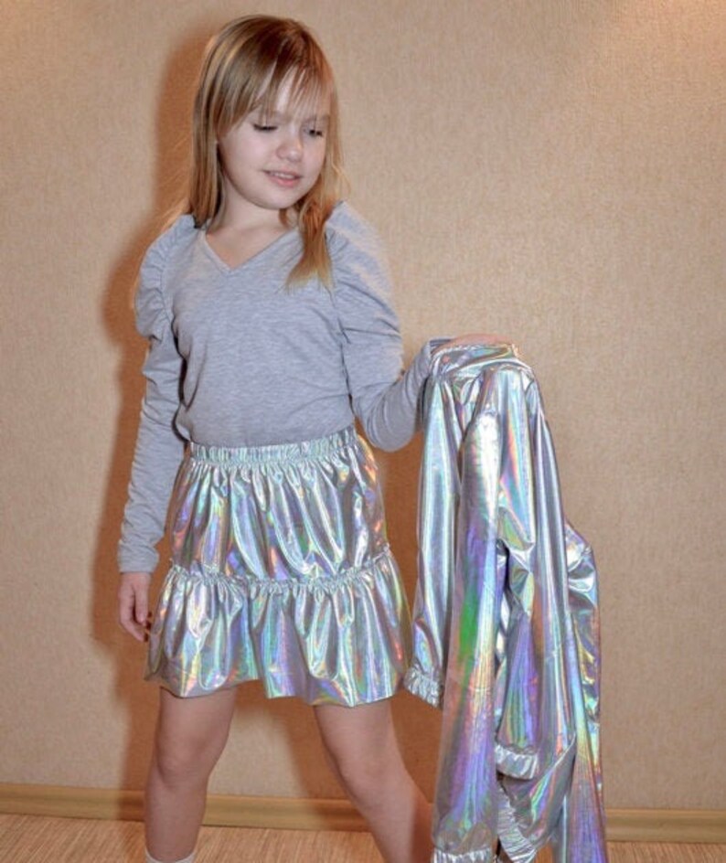 May include: A young person wearing a gray long-sleeved shirt with a silver iridescent skirt and a silver iridescent jacket.