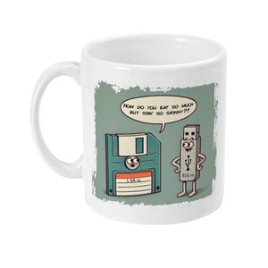 Puede incluir: Taza de cerámica blanca con una ilustración de dibujos animados de un disquete y una unidad USB. El disquete le dice a la unidad USB: "¿Cómo puedes comer tanto y seguir tan delgado?"