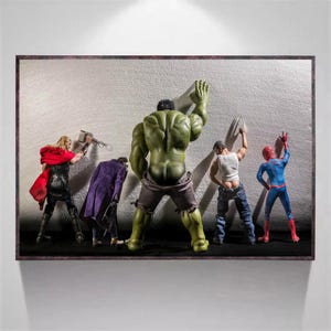 May include: A framed artwork featuring action figures of comic book characters. Thor holds a hammer, Hulk flexes, and Spider-Man poses. The figures are set against a textured white wall, creating a dynamic and playful scene.