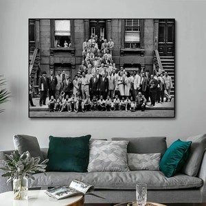 May include: Black and white photograph of a large group of people standing and sitting in front of a building. The people are all dressed in clothing from the 1950s and 1960s. The building is a brick building with a stoop and a window.