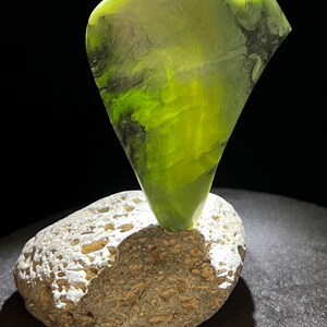 May include: A green jade stone sculpture in the shape of a bird perched on a gray and white rock.