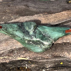 May include: A green stone pendant with a unique shape, attached to a brown leather cord with a cream-coloured knot.