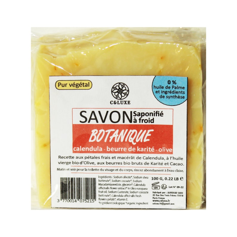 May include: A wrapped bar of botanical soap with a white label. The label reads "SAVON BOTANIQUE" and lists ingredients. The soap is yellow with visible orange flecks. The packaging states the soap is made with calendula, shea butter, and olive oil.