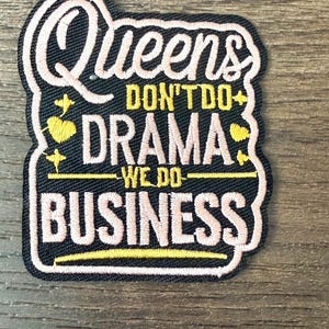 May include: Embroidered patch with the text "Queens Don't Do Drama We Do Business". The patch has a black background with pink and yellow accents. The text is in a stylized font.