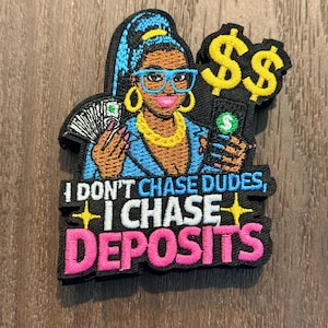 Op de afbeelding: Geborduurde patch met een vrouw met blauw haar, een bril en gouden sieraden, die geld en een telefoon met een dollarteken vasthoudt. De patch leest "I DON'T CHASE DUDES, I CHASE DEPOSITS" in witte en roze tekst.