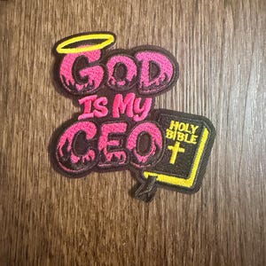 May include: Embroidered patch with the text "God Is My CEO" in pink and black. The patch includes a yellow halo, and a small black book with the words "Holy Bible" and a yellow cross.