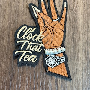 Może przedstawiać: Biały ceramiczny kubek z czarnym uchwytem i napisem "But First, Coffee" pogrubioną, czarną czcionką. Kubek jest umieszczony na rozmytym tle, sugerującym przytulne otoczenie. Kubek wydaje się mieć pojemność około 350 ml.